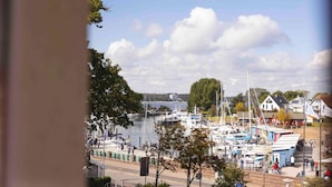 Ein Yachthafen mit vertäuten Booten, eine Uferpromenade und Gebäude im Hintergrund.