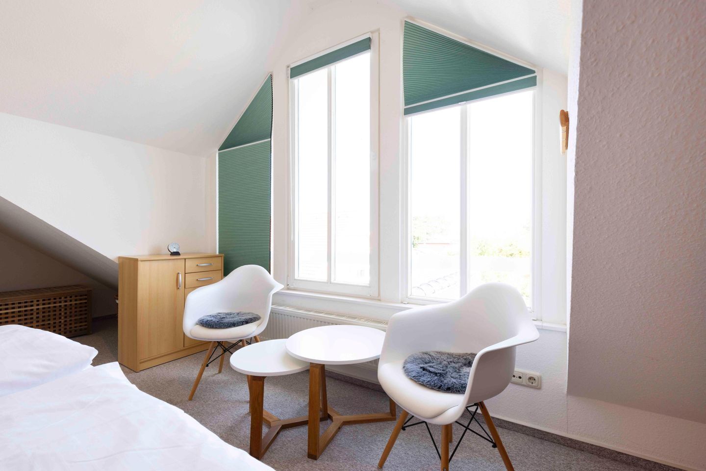 Quarto com uma cama, duas cadeiras brancas com almofadas fofas, um armário de madeira e uma janela com persianas verdes.
