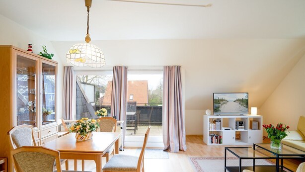 A spacious living room with a dining area, a TV stand, and a balcony with curtains. - (AMW1) Apartment Garbers/Thiele - Apartment "Garbers/Thiele" to 3 (Timmendorfer Strand)