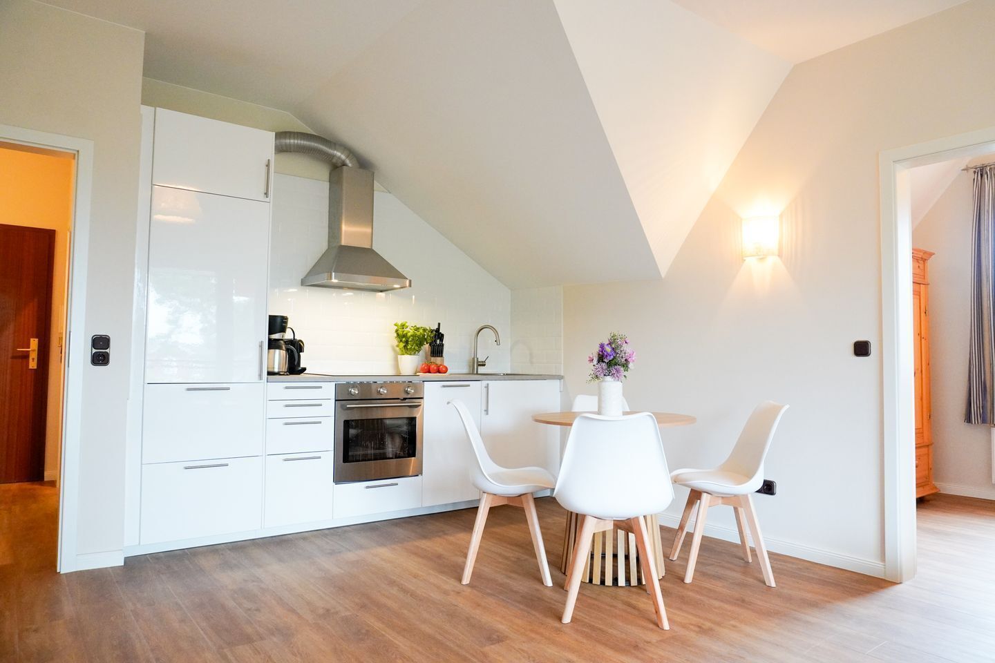 Une cuisine moderne avec des meubles blancs, un four en acier inoxydable et un coin repas avec des chaises blanches.