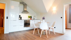 A modern kitchen with white cabinetry, a stainless steel oven, and a dining area with white chairs. - (STR74a) "Seaside Club" Vacation Rental - Seaside Club Vacation Rental for up to 4 (Timmendorfer Strand)