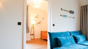 A room with a blue sofa, a lamp, a wooden dresser, and wall decorations including bird silhouettes and paddle-shaped items. - (STR74a) "Seaside Club" Vacation Rental - Seaside Club Vacation Rental for up to 4 (Timmendorfer Strand)
