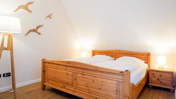 A room with a wooden bed, bedside lamps, and wall-mounted bird decorations. - (STR74a) "Seaside Club" Vacation Rental - Seaside Club Vacation Rental for up to 4 (Timmendorfer Strand)