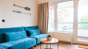 A room with a blue sofa, a small round table with a plant, and a window with curtains. - (STR74a) "Seaside Club" Vacation Rental - Seaside Club Vacation Rental for up to 4 (Timmendorfer Strand)