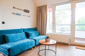 A room with a blue sofa, a small round table with a plant, and a window with curtains. - (STR74a) "Seaside Club" Vacation Rental - Seaside Club Vacation Rental for up to 4 (Timmendorfer Strand)