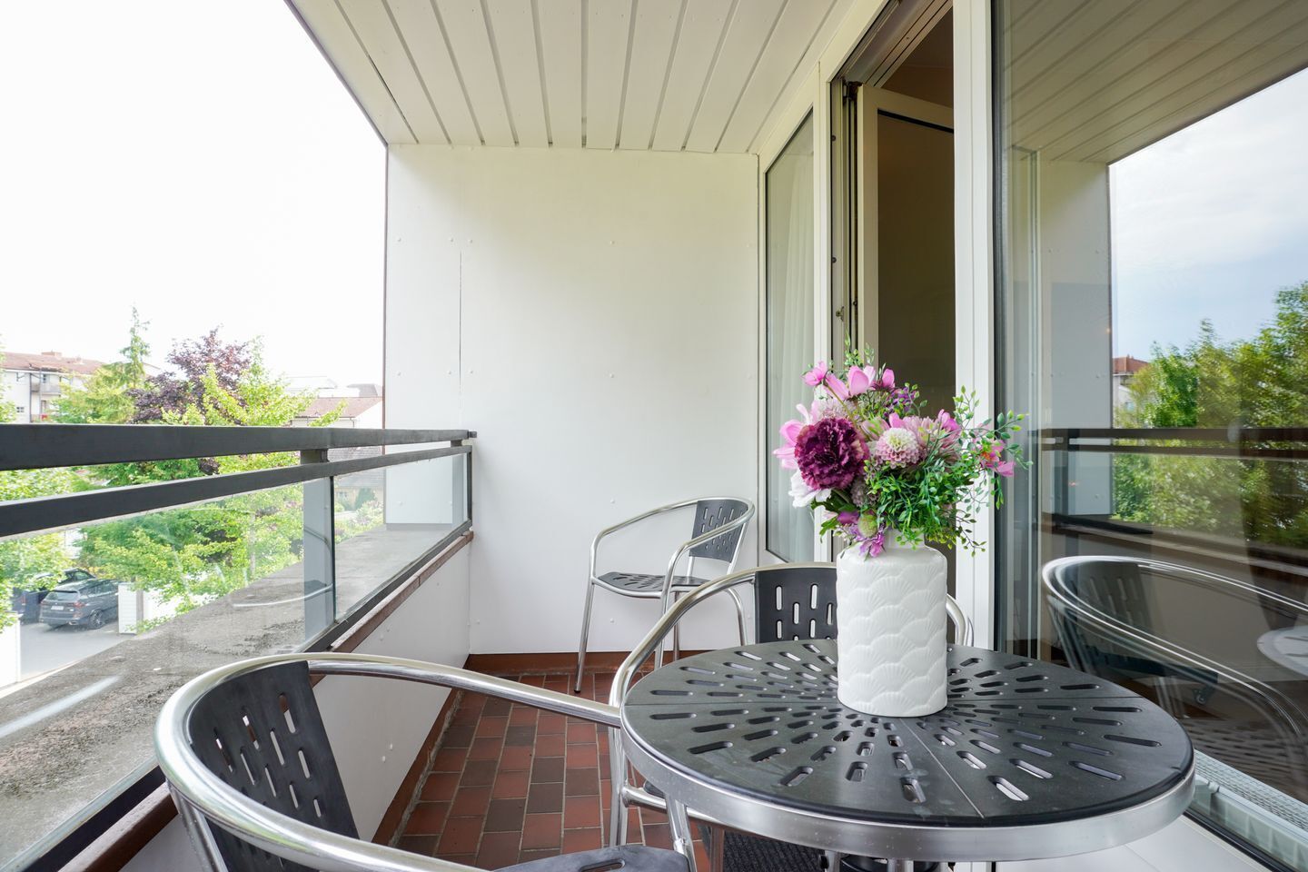 Un balcón con una mesa y sillas, un florero con flores y vistas al exterior.