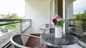 A balcony with a table and chairs, a vase with flowers, and a view of the outside. - (STR74a) "Seaside Club" Vacation Rental - Seaside Club Vacation Rental for up to 4 (Timmendorfer Strand)