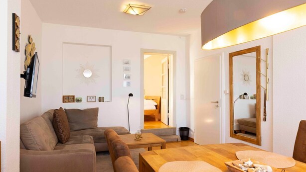 Een moderne woonkamer met een bank, een salontafel, een eettafel met placemats, een spiegel en een gang die naar een andere kamer leidt.
