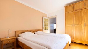 Een slaapkamer met een houten bed, een nachtkastje, een kledingkast en een deur naar een andere kamer.