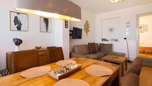 Een moderne woonkamer met een houten eettafel, een bank en een aan de muur bevestigde televisie.