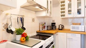 Een keuken met witte kastjes, een magnetron, een koffiezetapparaat en een fornuis.
