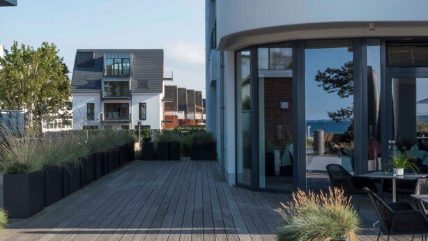 A rooftop terrace with a wooden deck, outdoor seating, and a view of the sea.
