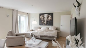 A modern bedroom with a bed, a chair, a TV, and a large elephant artwork on the wall.