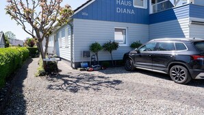 Una casa llamada 'HAUS DIANA' con un camino pavimentado, una camioneta SUV estacionada y un pequeño árbol.