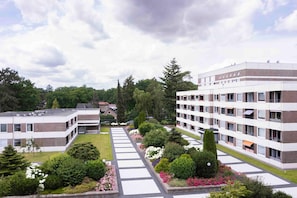 Un immeuble moderne à plusieurs étages, doté d’une cour intérieure et entouré de verdure et d’arbres.