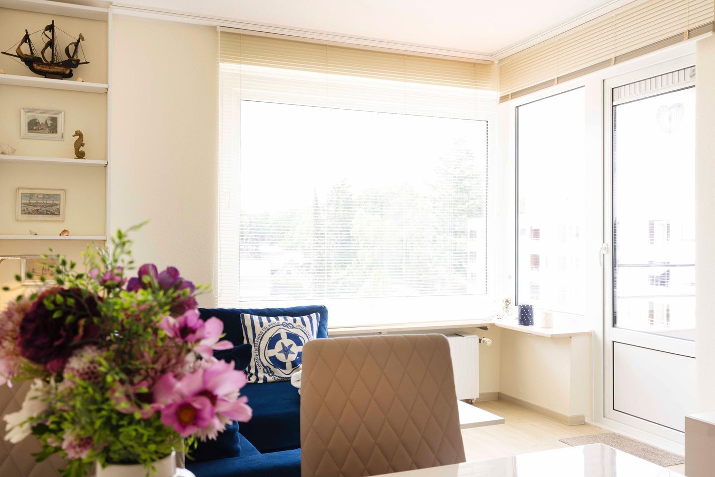 A modern living room with a blue sofa, a brown armchair, and a large window with blinds.