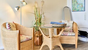 Una habitación con mobiliario de mimbre, una mesa de vidrio, una planta en maceta, un mapa en la pared y una lámpara.