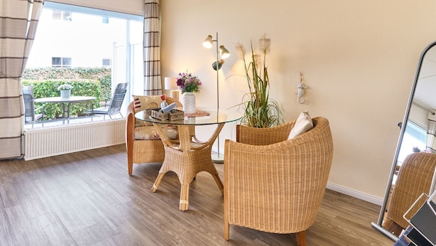 Una habitación con una mesa de vidrio, sillas de mimbre, una planta en maceta y vistas al exterior.