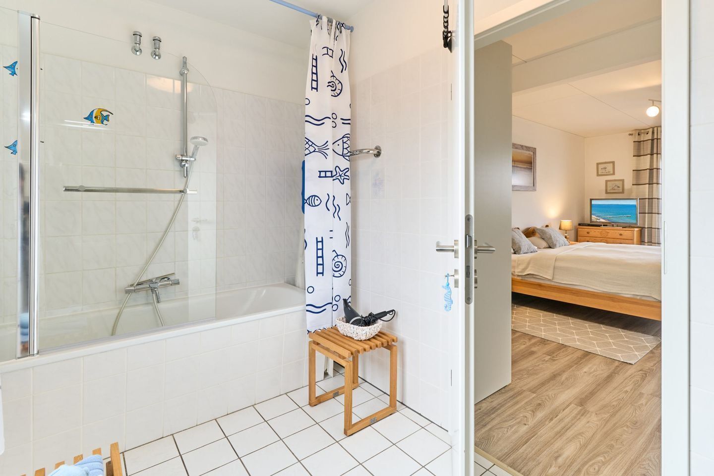Ein Badezimmer mit einer gläsernen Dusche, einem Holzschemel und einem Handtuchhalter.