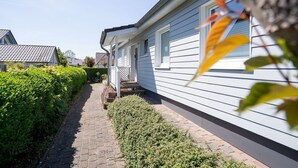Una casa residencial con un camino pavimentado, fachada blanca y un seto cuidado.