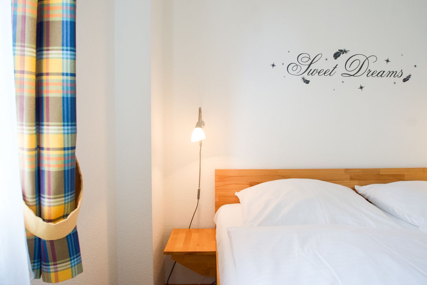 A hotel room with a bed, a nightstand with a lamp, and a wall with the text 'Sweet Dreams'.