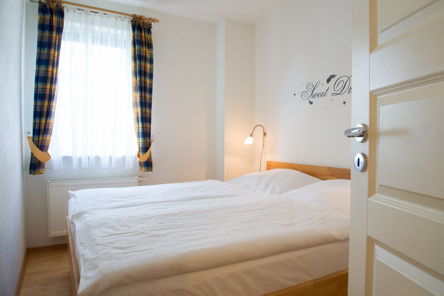 A hotel room with two beds, a window with plaid curtains, a bedside lamp, and a wall decoration.