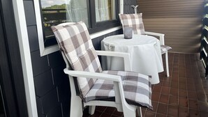 En uteplats med ett vitt bord och två stolar, var och en med kuddar i rutigt mönster.