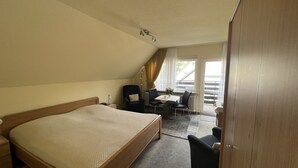 Ett hotellrum med en stor säng, ett skrivbord med två stolar, ett element och ett fönster med gardiner.