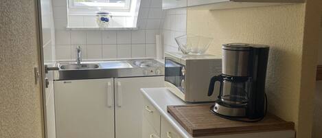 A compact kitchen with white cabinets, a built-in oven, a coffee maker, and a window above the sink.