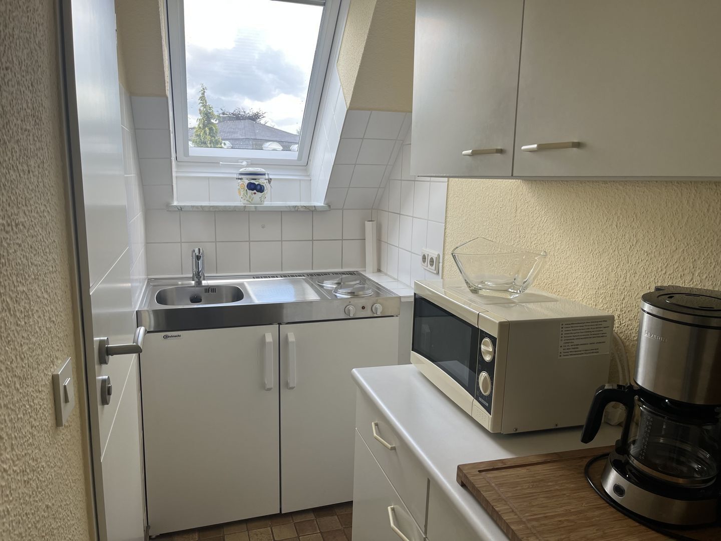 A compact kitchen with white cabinets, a built-in oven, a microwave, and a coffee maker.