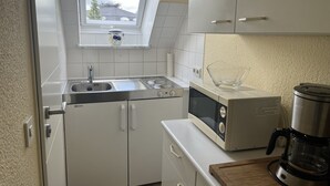 Ett kompakt kök med vita skåp, en inbyggd ugn, en mikrovågsugn och en kaffebryggare.