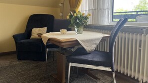 Ett mysigt rum med en mörkblå fåtölj, ett litet bord med en vit duk, en vas med gula blommor och ett element.