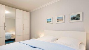 A bedroom with a bed, a wardrobe, and three framed pictures on the wall. - (TRA4) Holiday apartment "Hubertus "F*** - Holiday apartment "Hubertus" up to 3 persons (Timmendorfer Strand)