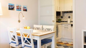 A compact kitchen with white cabinets, a tiled backsplash, and a small dining area with a table and chairs. - (TRA4) Holiday apartment "Hubertus "F*** - Holiday apartment "Hubertus" up to 3 persons (Timmendorfer Strand)