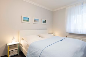 Une chambre à coucher avec un lit, une table de chevet, une lampe et trois tableaux encadrés accrochés au mur.