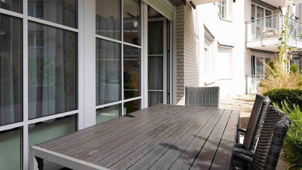 Patio esterno con tavolo e sedie, ampie finestre e vista sugli edifici vicini.