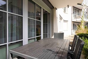 Un patio al aire libre con mesa y sillas, ventanas amplias y vistas a edificios cercanos.