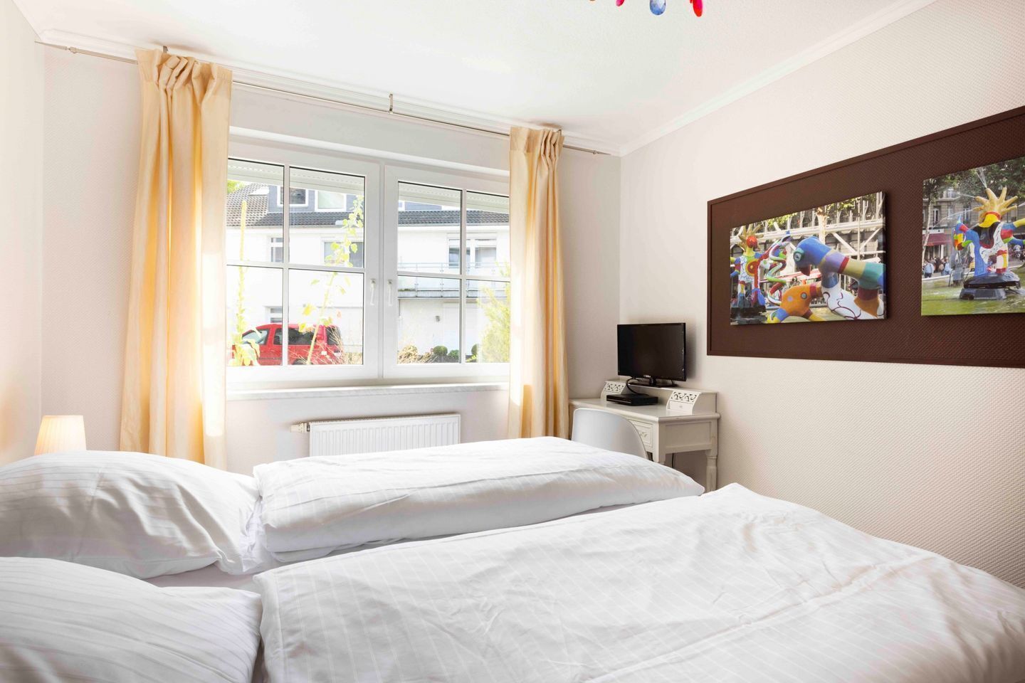A hotel room with two beds, a television on a small table, and a window with curtains.