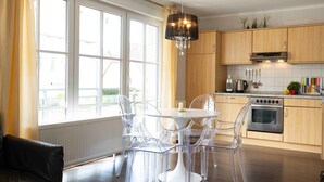 Una cucina moderna con mobili in legno, un forno in acciaio inossidabile e un'area pranzo con tavolo bianco e sedie trasparenti.