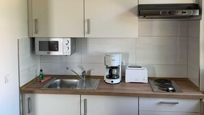 A compact kitchenette with a microwave, coffee maker, toaster, and a small stove. - (STR123b) Holiday apartment "Strandhotel" - App. 24 - Holiday apartment "Strandhotel" - (Timmendorfer Strand)