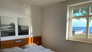 A bedroom with a bed, a window with a view of the sea, and two framed pictures on the wall. - (STR123b) Holiday apartment "Strandhotel" - App. 24 - Holiday apartment "Strandhotel" - (Timmendorfer Strand)