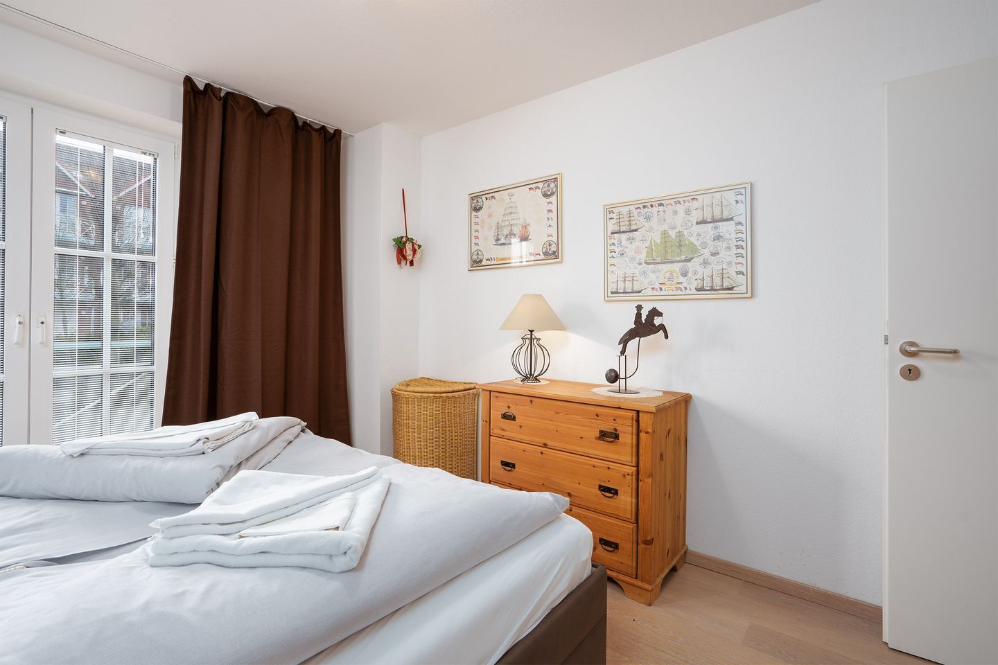 A bedroom with a bed, a wooden dresser, a lamp, and two framed pictures on the wall.
