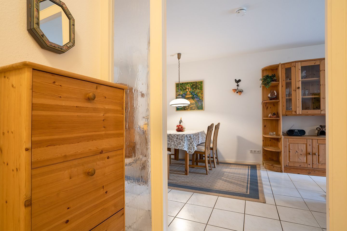 A room with a wooden dresser, a dining table with chairs, a painting on the wall, and wooden cabinets.