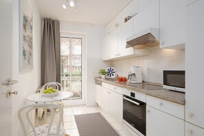 Une cuisine moderne avec des meubles blancs, un four encastré, un four à micro-ondes et une machine à café.