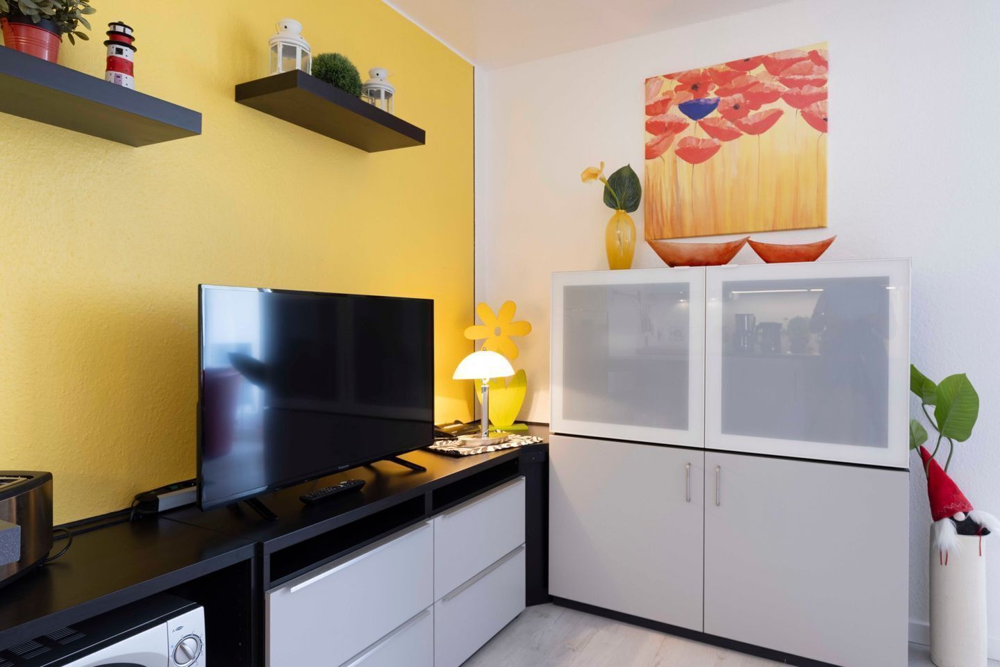 A compact kitchen with a flat-screen TV, a white refrigerator, and a yellow wall.