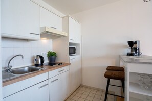Una cocina moderna con armarios blancos, un lavamanos de acero inoxidable, una cafetera y un taburete de bar.