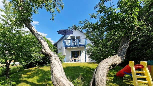 Una casa con balcón azul, rodeada de árboles y un jardín con césped.