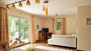 Una sala de estar con un sofá, un televisor, un aparador de madera y una zona de comedor con una mesa y sillas.