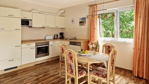 Una cocina con armarios de madera, un microondas, un tostador y un lavabo. Hay una mesa de comedor con sillas y un florero con flores.