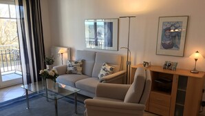 Una sala moderna con sofá, sillón, mesa de centro de vidrio y un mueble con lámpara.